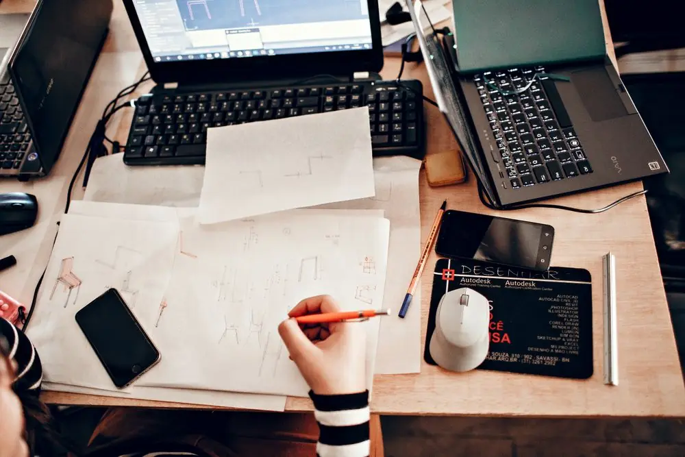 Overhead perspective of design plans, digital interface wireframes, and drafting tools on a desk