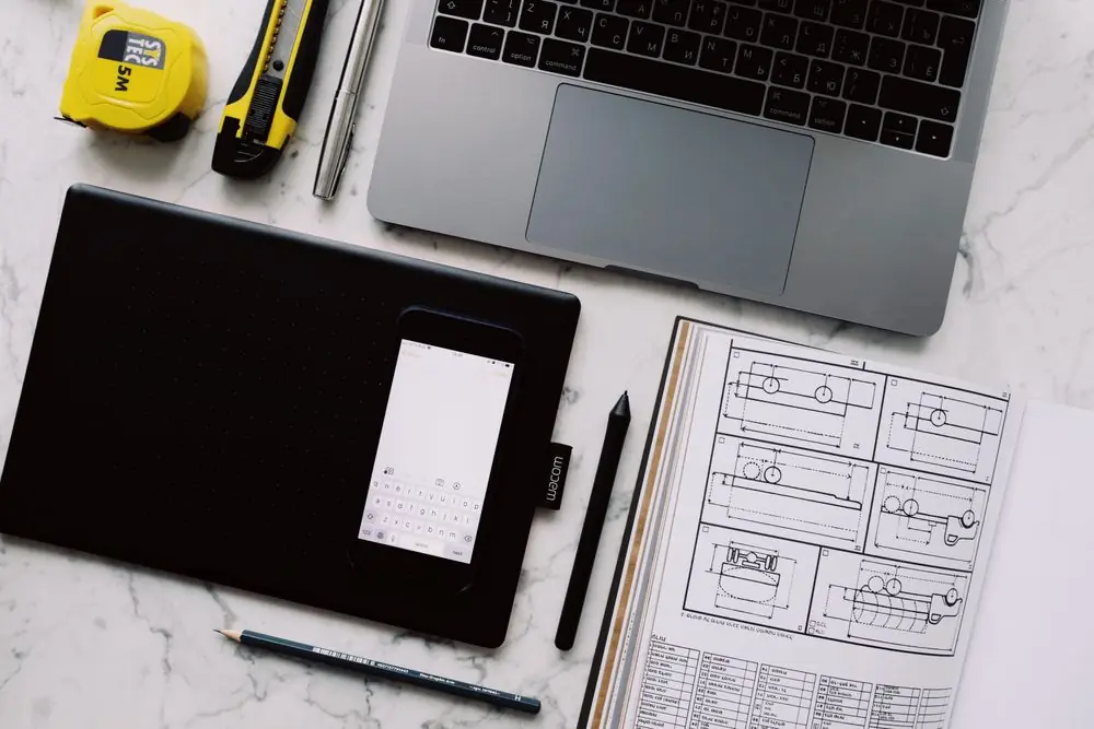 Designer desk with notebook sketches, stylus, ruler, and digital device demonstrating careful interface composition